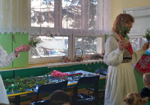 Dzieci siedzą przy stolikach, wykonują palemki wielkanocne, Panie z Koła Ludowego pomagają Dzieciom w wykonaniu palemek.