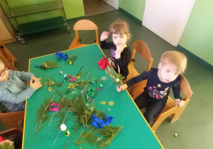 Dzieci siedzą przy stolikach, wykonują palemki wielkanocne.