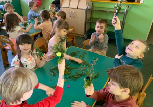 Dzieci siedzą przy stolikach, wykonują palemki wielkanocne.