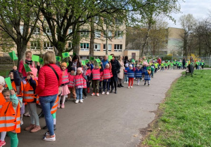 Dzieci niosąc zielone fagi, wraz z opiekunami maszerują w pobliskim parku.