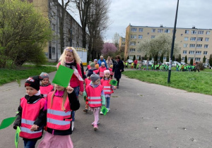 Dzieci niosąc zielone fagi, wraz z opiekunami maszerują w pobliskim parku.