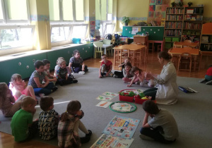 Pani dietetyk siedzi z dziećmi na dywanie, przy rozłożonych obrazkach zdrowej i niezdrowej żywności.