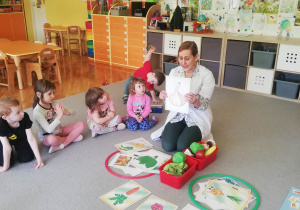 Pani dietetyk siedzi z dziećmi na dywanie, przy rozłożonych obrazkach zdrowej i niezdrowej żywności.