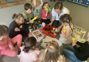 Pani dietetyk siedzi z dziećmi na dywanie, przy rozłożonych obrazkach zdrowej i niezdrowej żywności.