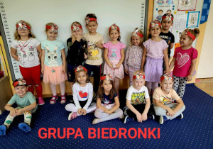 Dzieci stoją i siedzą w grupie, która nazywa się Biedronki.