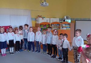 Dzieci stoją w kole, ubrane na galowo, śpiewają hymn Polski