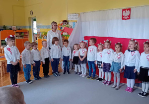 Dzieci stoją w kole, ubrane na galowo, śpiewają hymn Polski