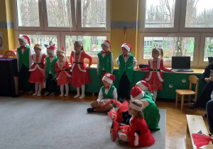 Dzieci z grupy Liski stoją w półokręgu wraz z siedzącym obok Rodzicami.