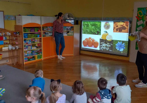 Dzieci siedzą w kole na dywanie, słuchając prezentacji o historii herbaty.