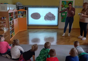 Dzieci siedzą w kole na dywanie, słuchając prezentacji o historii herbaty.