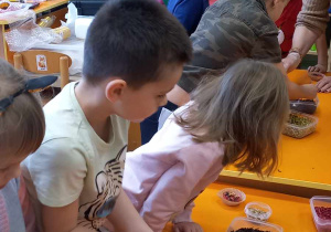 Dzieci stoją dookoła stołów, komponując swoje napoje herbaciane.