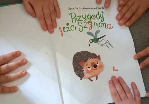 Dzieci siedzą na dywanie, dotykają ksiązkę.