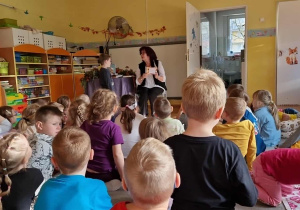 Dzieci siedzą na dywanie przed poetką Panią Urszulą Kowalską, która czyta dzieciom swoje utwory.