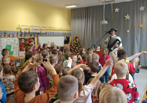 Góral Szczepan gra kolędy na akordeonie przed tańczącymi dziećmi.
