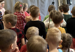 Góral Szczepan gra kolędy na akordeonie przed stojącymi dziećmi.
