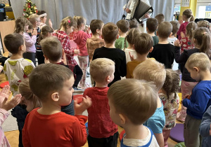 Góral Szczepan gra kolędy na akordeonie przed stojącymi dziećmi.