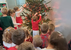 Dzieci ubierają choinkę w piernikowe ozdoby w szatni przedszkola.