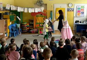 Troje dzieci przebrane za postaci z Lodowej Krainy tańczą z panią Natalią na środku sali, przed nimi siedzą pozostałe dzieci.
