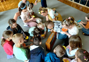 Dzieci siedzą na dywanie i obserwują pszczoły w edukacyjnym ulu.