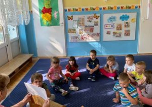 Biblioterapia w grupie I. Dzieci siedzą w kole. Nauczycielka pokazuje ilustrację.