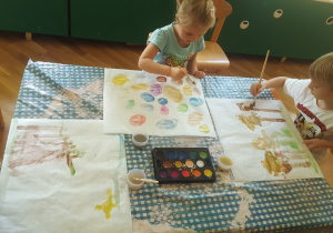 Plastykoterapia w grupie 4. Na zdjęciu widzimy dzieci malujące farbami akwarelowymi.