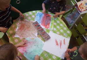 Plastykoterapia w grupie 4. Kilkoro dzieci siedzi przy stoliku i suchymi pastelami rysuje na kwadratowych kartonach.