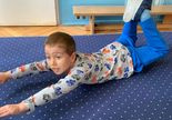 Terapia ręki w grupie 1. Chłopiec leży na podłodze na brzuchu. Ma wyciągnięte i uniesione do góry ręce i nogi.
