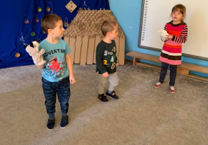 Teatroterapia w grupie 1. Troje dzieci stoi na dywanie. Mają kukiełki.