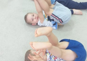 Grupa 5. Grupa dzieci leży na dywanie na plecach, przenosząc nogi za głowę.