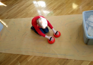 Dziecko kreśli kredowym korektorem do rysowania na dużym arkuszu papieru.