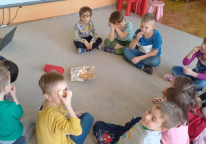 Biblioterapia grupa 5. Grupa dzieci siedzi na dywanie, słuchając bajki "O Piernikarzu i jego córce Katarzynie" z okazji Dnia Piekarzy i Cukierników.