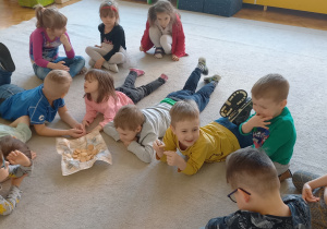 Biblioterapia grupa 5. Grupa dzieci siedzi na dywanie, słuchając bajki "O Piernikarzu i jego córce Katarzynie" z okazji Dnia Piekarzy i Cukierników.