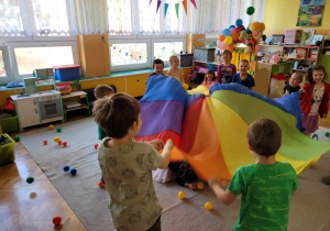 Choreoterapia grupa 5. Zabawa dzieci w wiosenny deszczyk z wykorzystaniem chusty animacyjnej oraz kolorowych piłeczek.