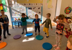 Choreoterapia w grupie 1. Taniec dinozaurów. Dzieci stoją na dywanie, przed każdym dzieckiem leży kolorowy krążek.