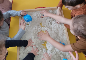 Plastykoterapia grupa 3. Na zdjęciu widać grupę dzieci wykopującą szczątki dinozaura z piasku.