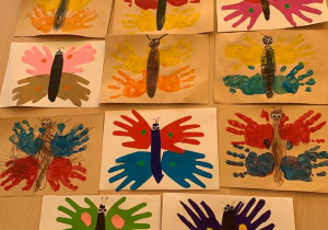 Plastykoterapia w grupie 1. Zdjęcie przedstawia kolorowe motyle. Dzieci młodsze stemplowały dłońmi pomalowanymi farbą, a starsze odrysowywały dłonie na kolorowym papierze, wycinały i naklejały na karton.