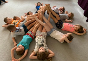 Gr. 1. Dzieci leżą na plecach na dywanie. Tworzą piramidę z nóg.