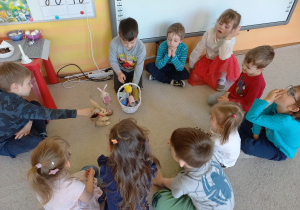 Biblioterapia grupa 5. Dzieci siedzą w kółku na dywanie, słuchając bajki o zajączkach.