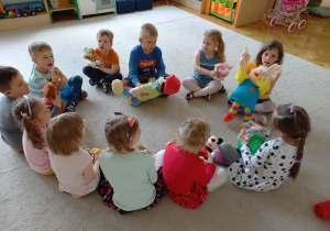 Teatroterapia grupa 5. Na zdjęciu widać siedzące na dywanie dzieci, odgrywające role lalek i piłek.