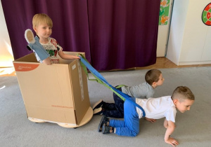 Gr.1. Teatroterapia. Dzieci odtwarzają scenkę z opowiadania Anaruk chłopiec z Grenlandii. Na zdjęciu w saniach z kartonu siedzi chłopiec. Sanie zaprzężone w dwa "pieski".