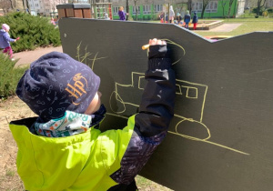 Terapia ręki gr. 1. Chłopiec rysuje kredą na tablicy w ogrodzie przedszkolnym.