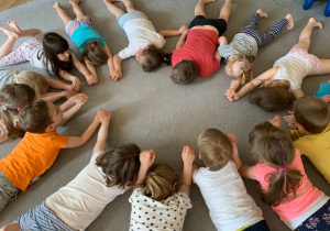 Gr. 1. Dzieci leżą na brzuchu na dywanie. Ręce wyciągnięte przed siebie, głowy uniesione.