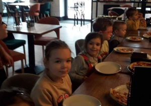 Dzieci siedzą przy stole w pizzerii, oczekując na pizzę.