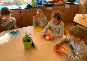 Dzieci siedzą przy stoliku i jedzą pizzę.