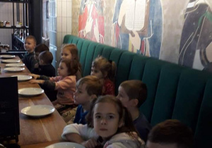 Dzieci siedzą przy stole w pizzerii, oczekując na pizzę.