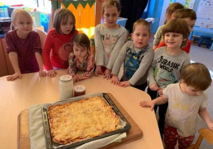 Dzieci stoją przy stoliku, na którym na tacy leży upieczona pizza.