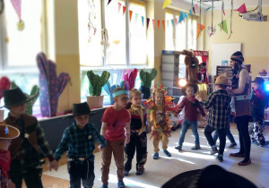 Dzieci w kółku tańczą na Balu Karnawałowym.