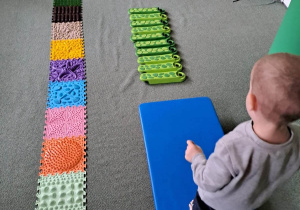 Chłopiec przechodzi przez kolorowe elementy, ułożone na dywanie.
