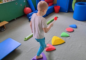 Chłopiec przechodzi przez kolorowe elementy, ułożone na dywanie.