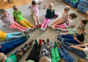 Dzieci siedzą na dywanie w kole, mają na stopach kolorowe skarpetki.